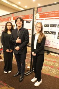 Three people smile in front of posters.